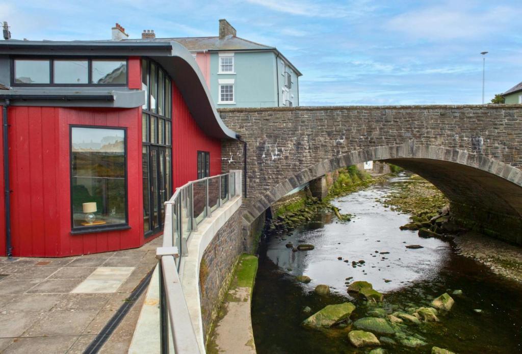 a bridge over a river next to a red building at Ger Y Llanw Aberaeron in Aberaeron