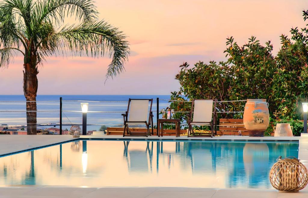 a pool with chairs and a palm tree and the ocean at Cretan Dream Villa in Georgioupolis