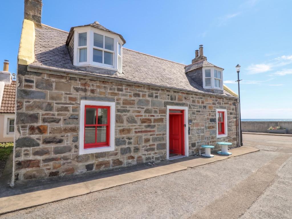an old stone building with red doors and windows at Dookers' Hoose in Buckie