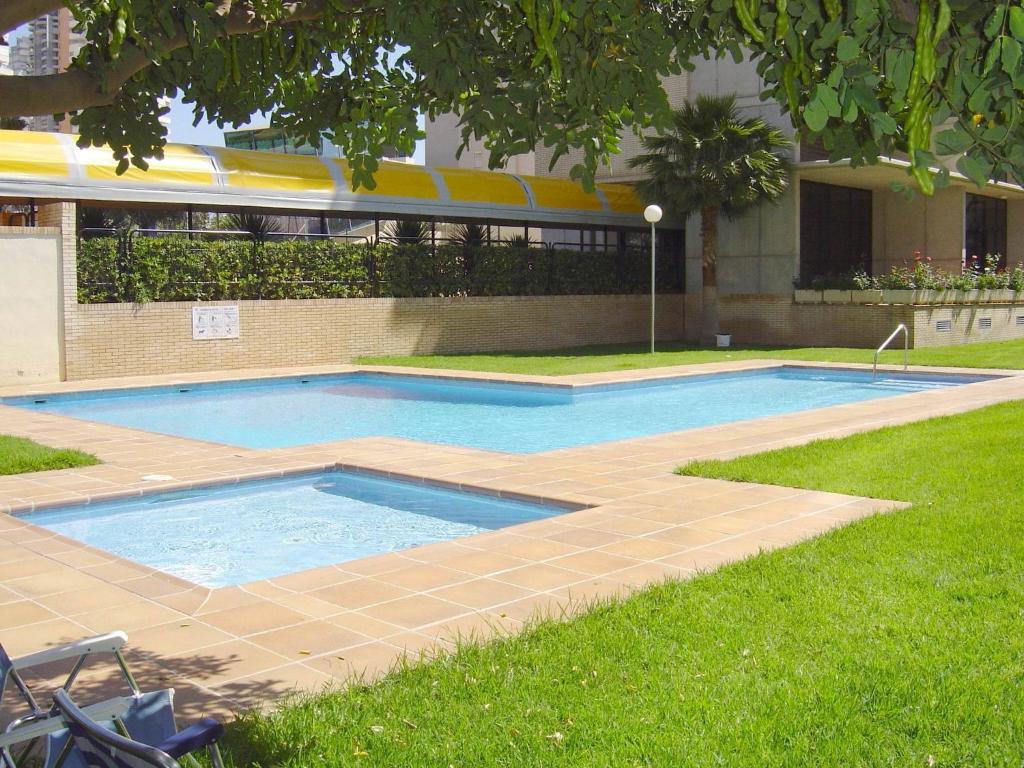 Hotel Apartamentos Torre Ipanema, a swimming pool in the grass next to a building at Apartamentos Torre Ipanema in Benidorm
