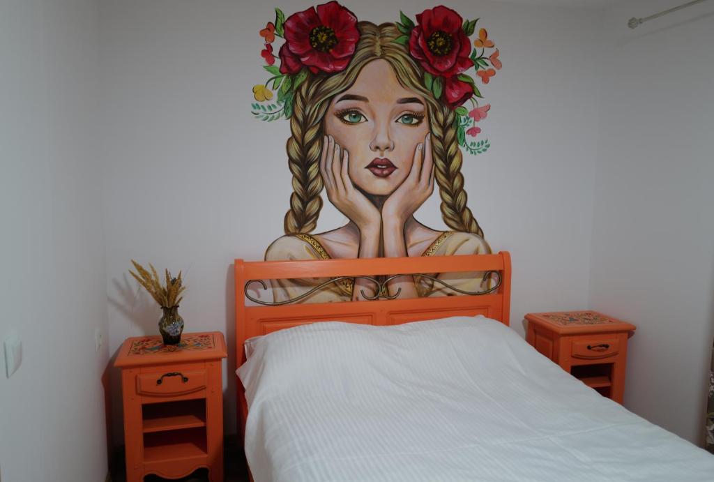 a bedroom with a painting of a woman with flowers on the wall at Raiul Sânzienelor in Sărata-Monteoru
