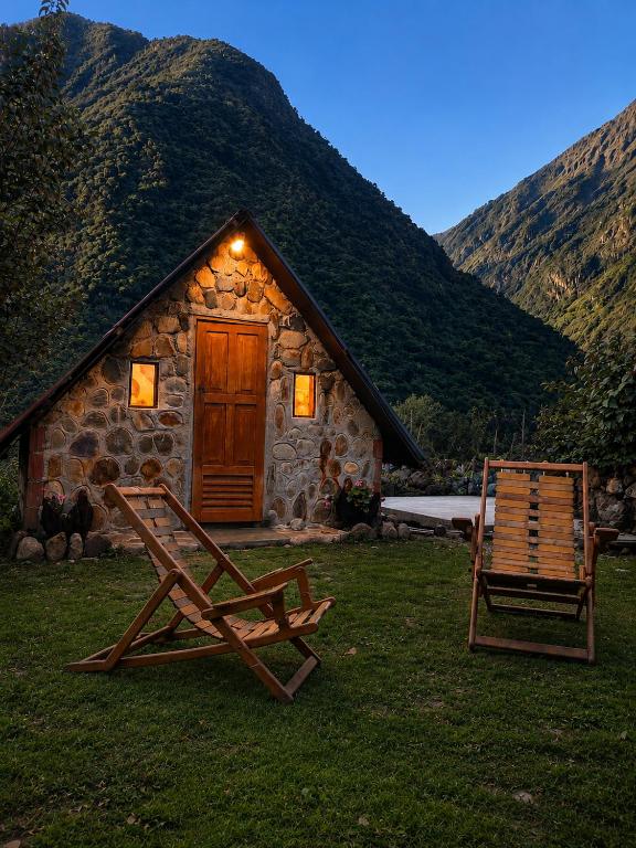 two chairs sitting in front of a stone cabin at Ebenezer Salkantay Huts in Colcapampa