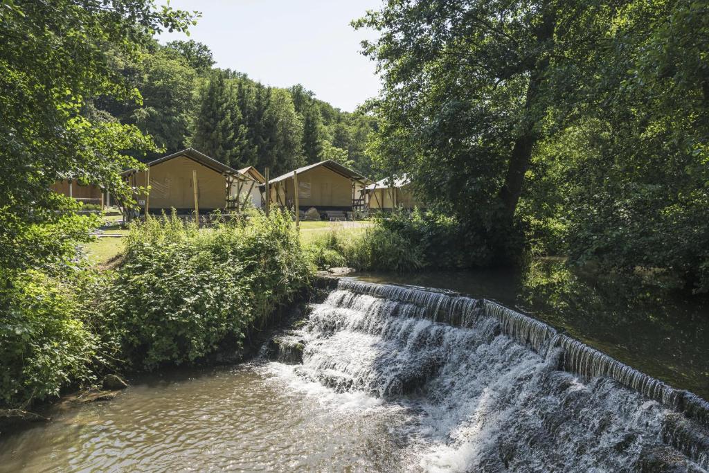 a waterfall in front of a river with houses at Landal Namur Nature in Gesves