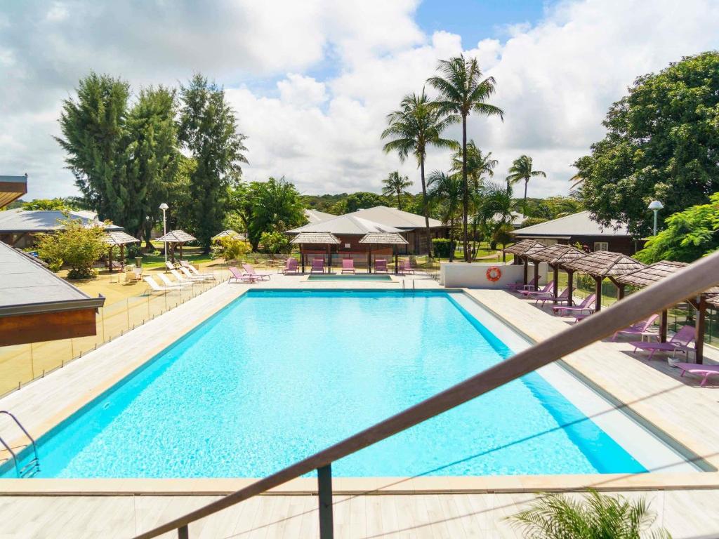 a swimming pool at a resort with palm trees at Hotel Mercure Kourou Ariatel in Kourou