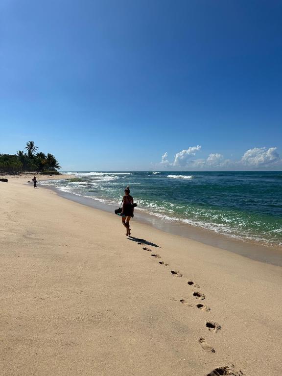 a woman walking on the beach with footprints in the sand at Sri Residence in Kamburugamuwa