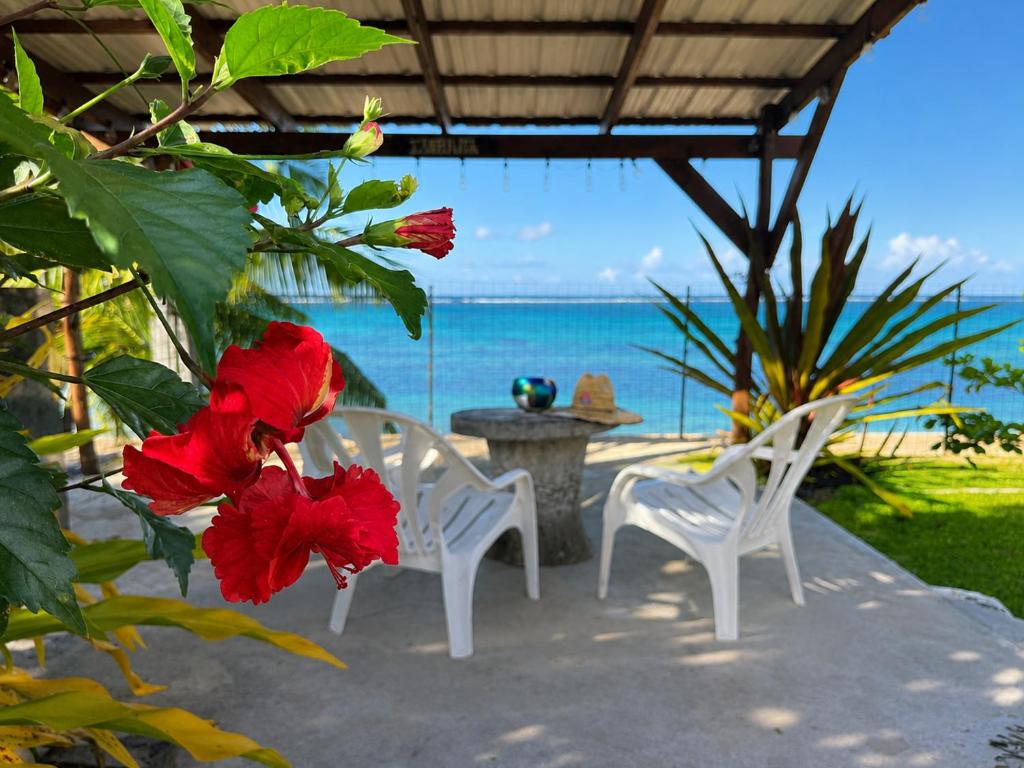 a patio with two white chairs and a table and red flowers at PK 35 in Apomaoro
