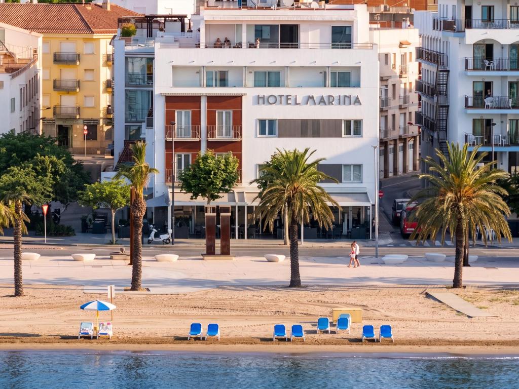 a beach with chairs and palm trees and buildings at Hotel Marina in Roses
