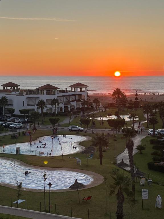a sunset over a park with a swimming pool and the ocean at Beachfront Apartment in Assilah, Private Solarium, 4 Pools, Secure Residence, WiFi, Parking in Asilah