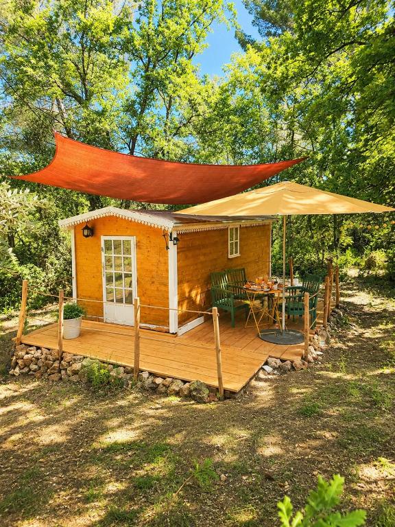 a house with a deck with a table and an umbrella at Roulotte nature in Salernes
