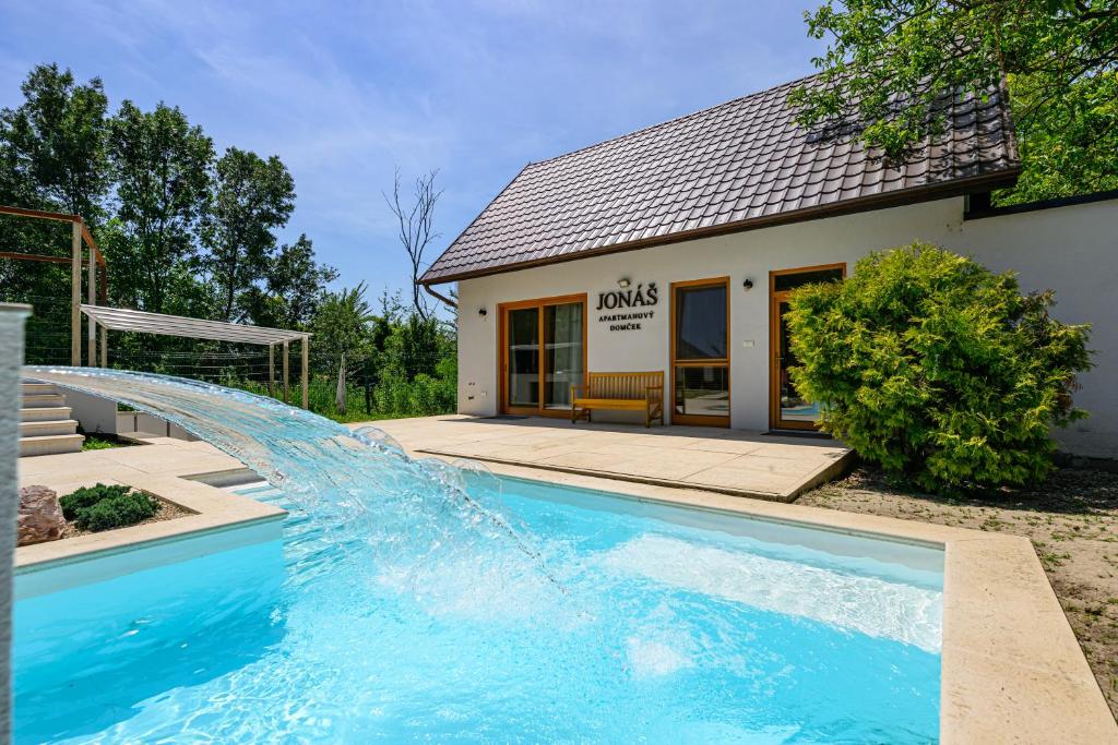 a swimming pool with a waterfall in front of a house at Penzión Walter in Veľké Úľany
