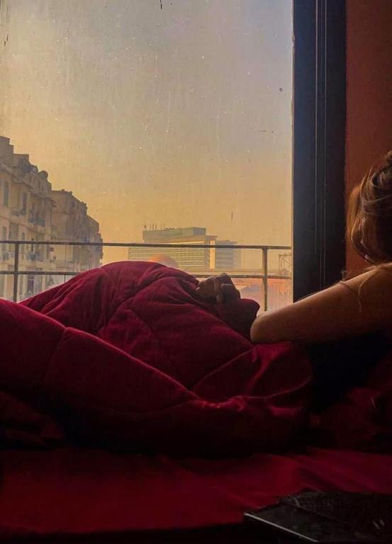 a woman laying in a bed under a blanket looking out a window at AL Waha Cairo Hotel in Cairo