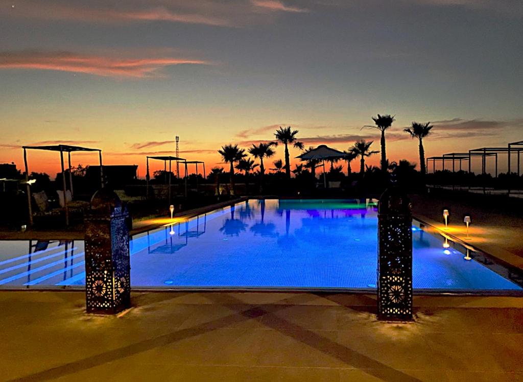 a large blue swimming pool with palm trees at sunset at Bab Sma in Oumnas