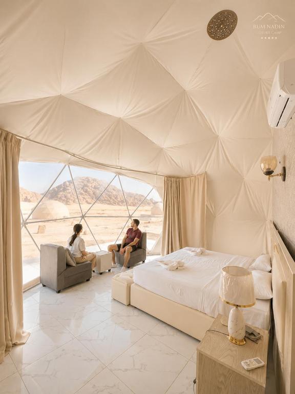 a bedroom with a bed and two people sitting in a tent at RUM NADINE LUXURY CAMP & Bubbles Hotel in Wadi Rum