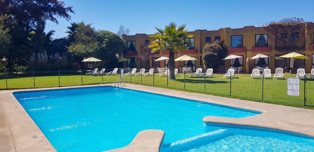 a swimming pool with chairs and a building in the background at Stellamar Apart Hotel in La Serena