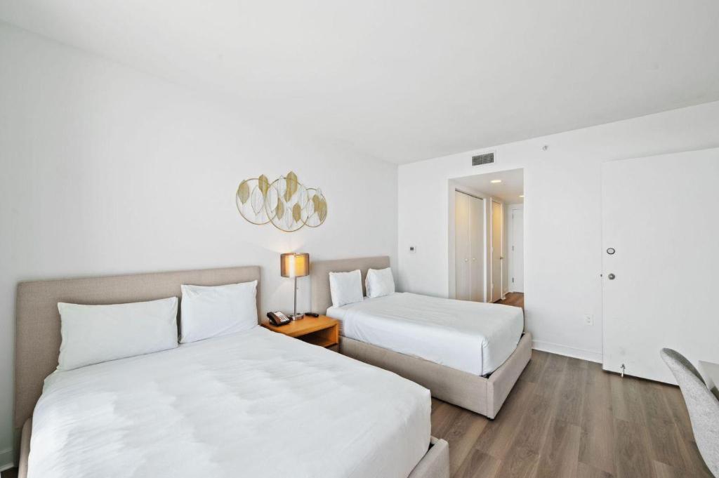 a white bedroom with two beds and a chandelier at Upper Studio Stunning Intracoastal Views in Hallandale Beach