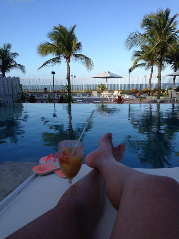 a man laying on the edge of a swimming pool with a drink at In Mare Bali Residencial Resort in Pium de Cima