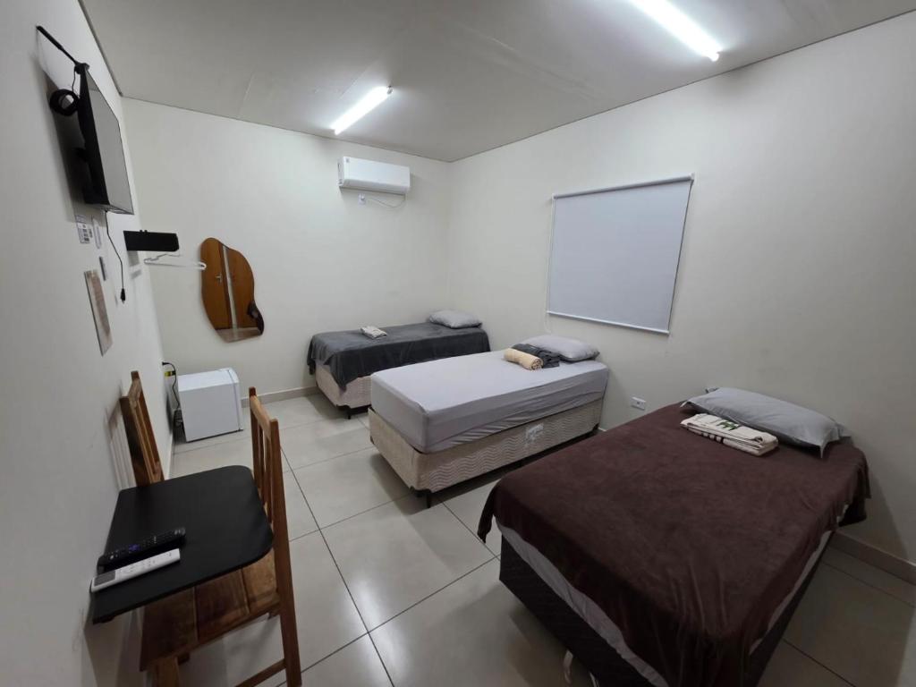 a room with two beds and a desk and a white wall at Suítes Caminho do Pantanal in Aquidauana