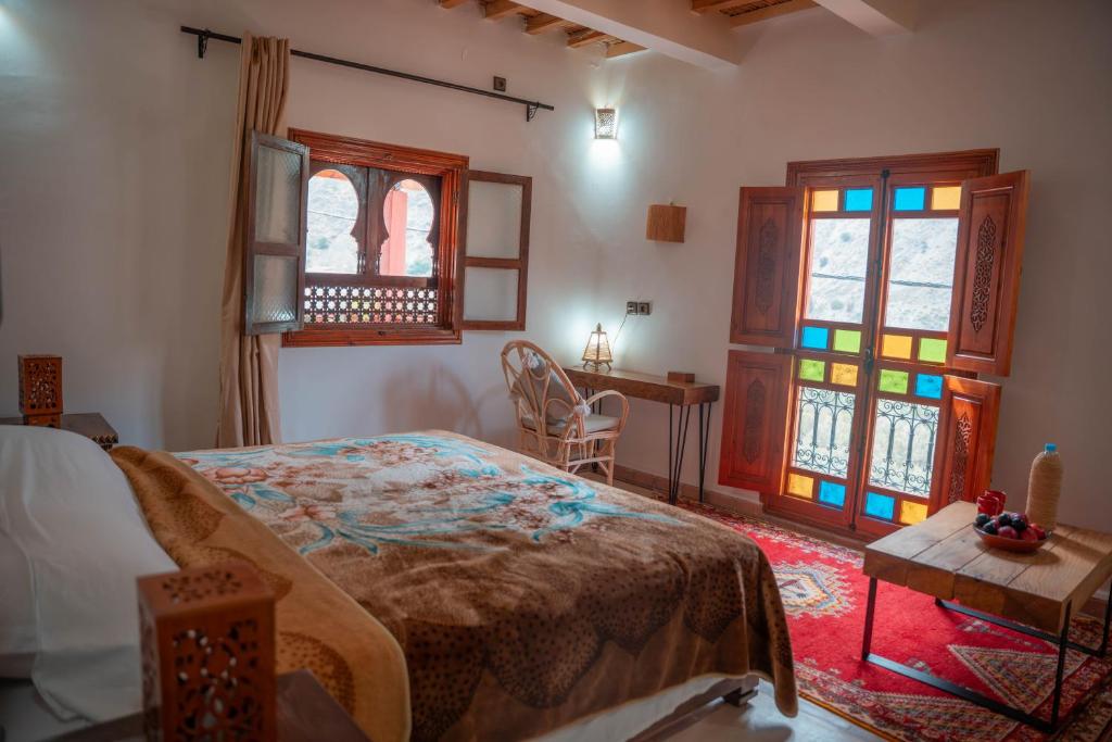 a bedroom with a bed and a table and windows at Ijoukak Berber HomeStay in Ijjoukak