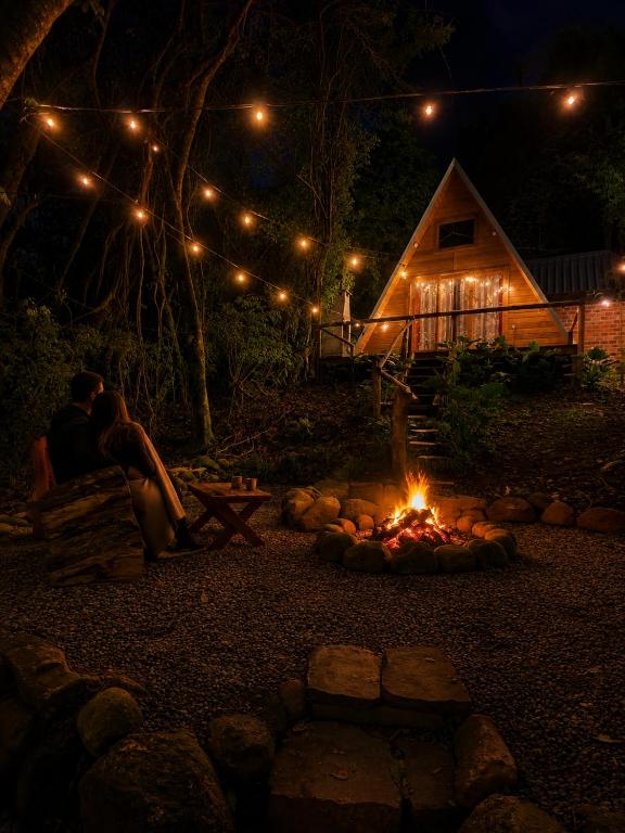 a couple sitting in front of a fire pit at night at Cabana Cipó in Passo Fundo