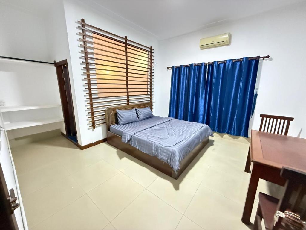a bedroom with a bed and a desk and blue curtains at White Castle in Siem Reap