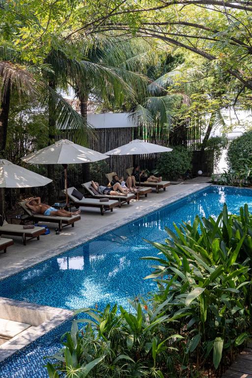 a swimming pool with people sitting on chairs and umbrellas at Pippali Boutique Hotel in Kampot