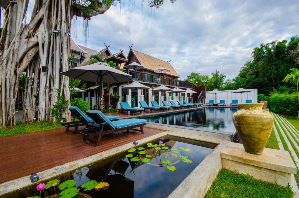 a pool with chairs and an umbrella next to a house at Buri Sriping Riverside Resort & Spa in Chiang Mai