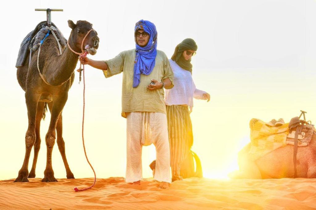 a man standing next to a horse in the desert at Erg Chebbi Dunes Desert Camp in Merzouga
