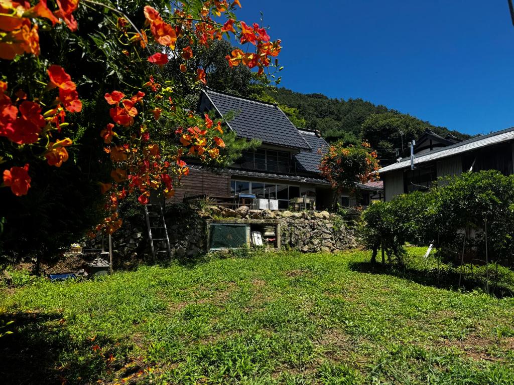 ein Haus mit einem Baum mit roten Blüten im Garten in der Unterkunft MEKIKI古民家 yorimichi in Yamanashi