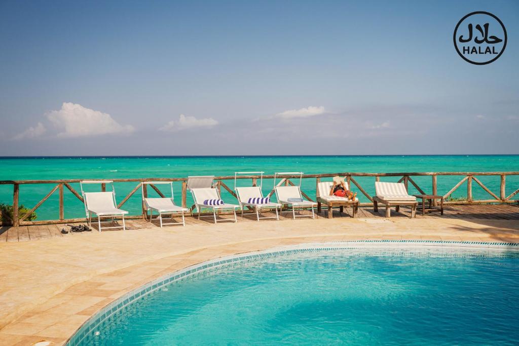 a pool with chairs and the ocean in the background at Tanzanite Beach Resort and Spa in Nungwi