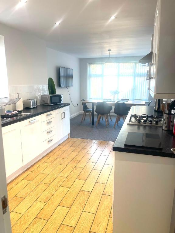 a kitchen with white cabinets and a wooden floor at Spacious airy modern private detached house in Beeston