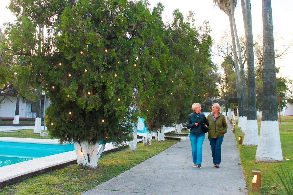 two older women walking down a sidewalk next to a tree at HOTEL OASIS Matehuala in Matehuala