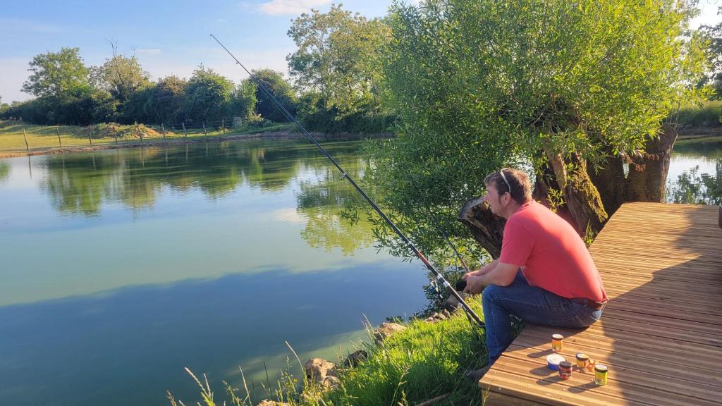 a man sitting on a deck fishing on a lake at Paradis nature dans Le PERCHE - Vue, Confort, Pêche, Étang, Salle de Sport, à 5min Ville & Gare in Belhomert-Guéhouville