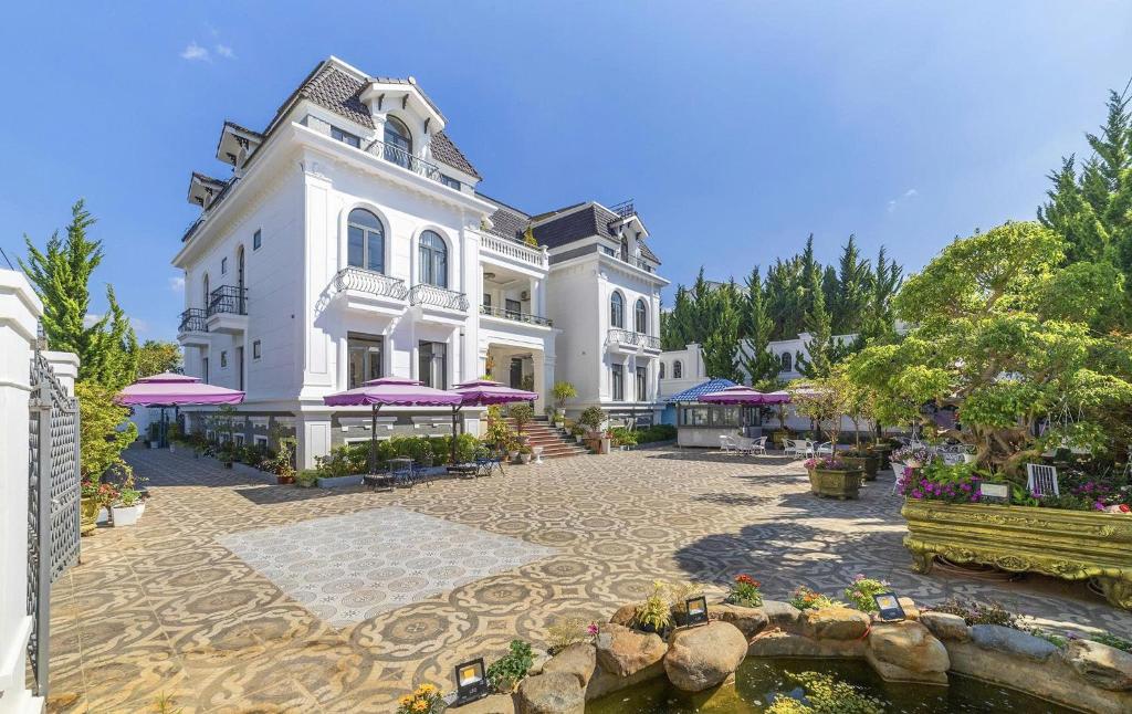 a large white building with purple umbrellas in a courtyard at Maro Luxury Boutique Villa - hotel in Da Thanh