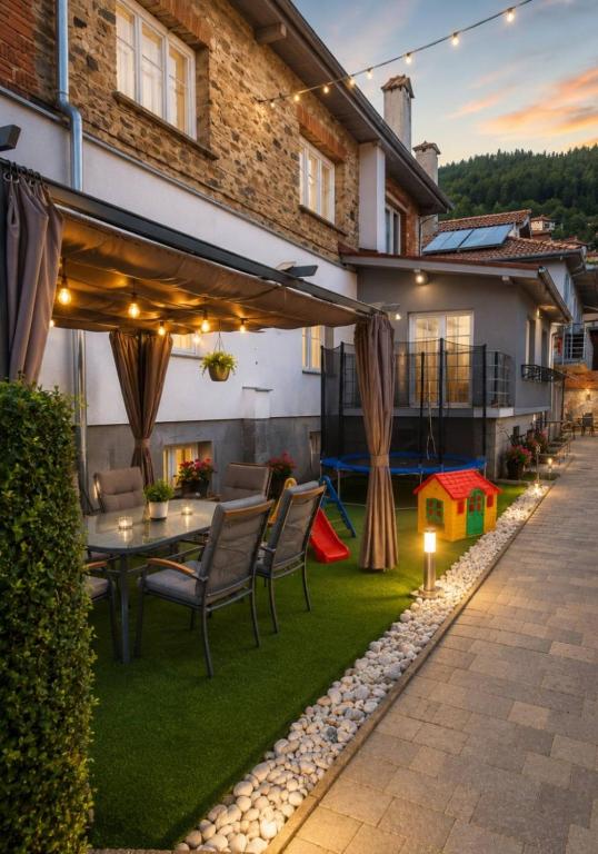 a patio with a table and chairs and a house at Къща за гости Сънрайс Чепеларе in Chepelare