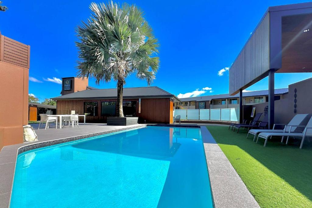 a swimming pool in front of a building with a palm tree at Quality Hotel City Centre in Coffs Harbour