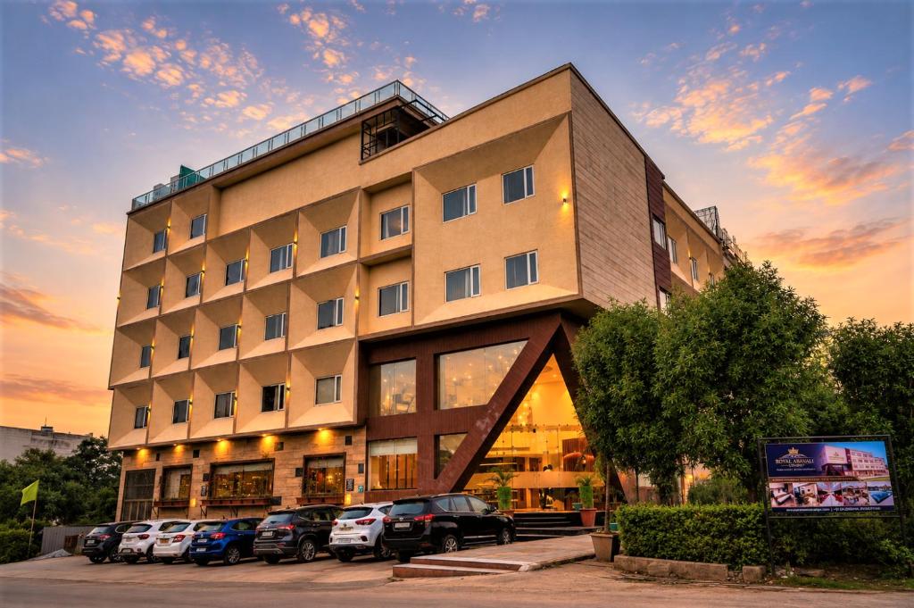 a building with cars parked in a parking lot at Hotel Royal Aravali in Udaipur
