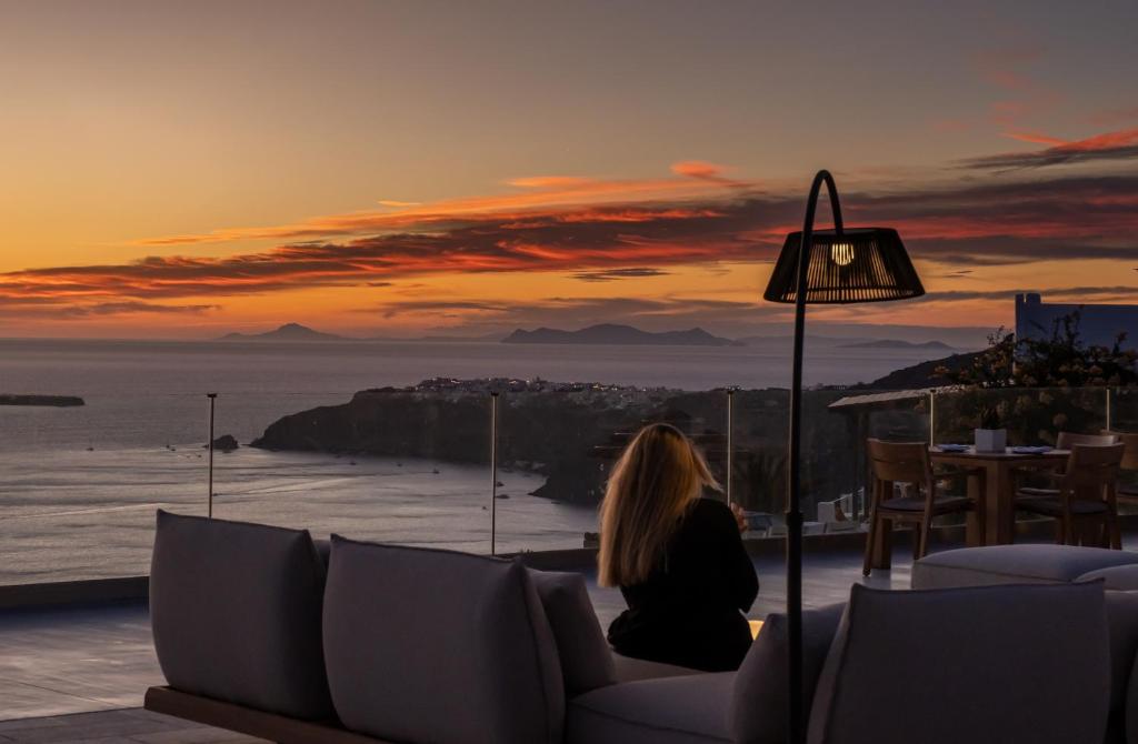 a woman sitting on a couch watching the sunset at Xenones Filotera in Imerovigli