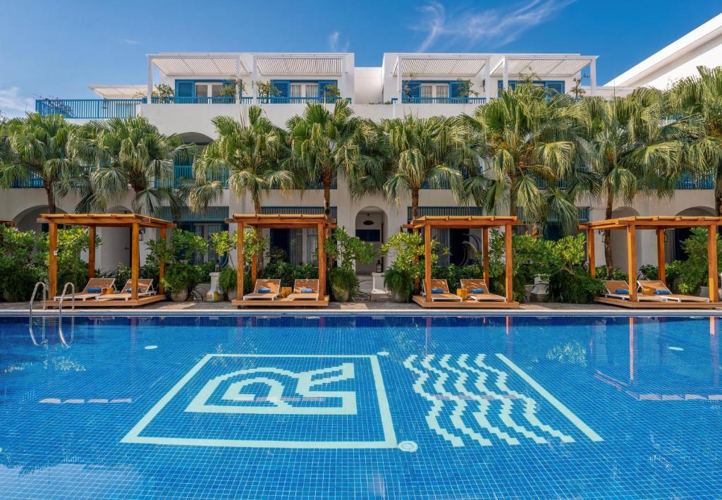 A resort pool viewed from the water, with palm trees, curtained cabanas and loungers along the far side.