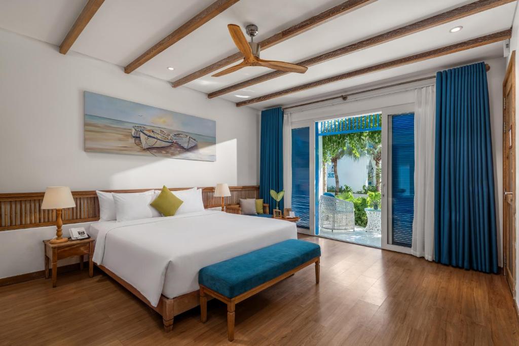A bright guest room with a king bed, wood floors, exposed ceiling beams, and a garden-facing opening.