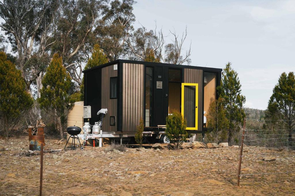 a tiny house with a yellow door in a field at Raya and Aiden Farm House by Tiny Away in Cooma