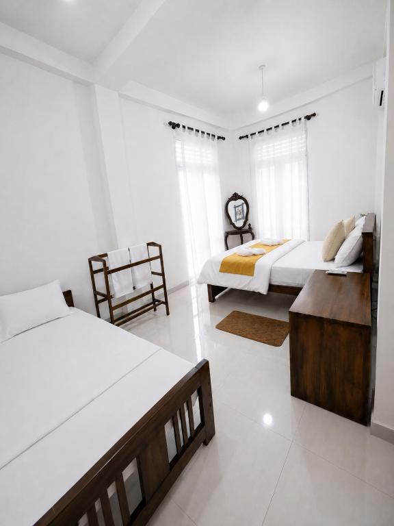 a white bedroom with two beds and a table at Bliss Stay in Katugastota