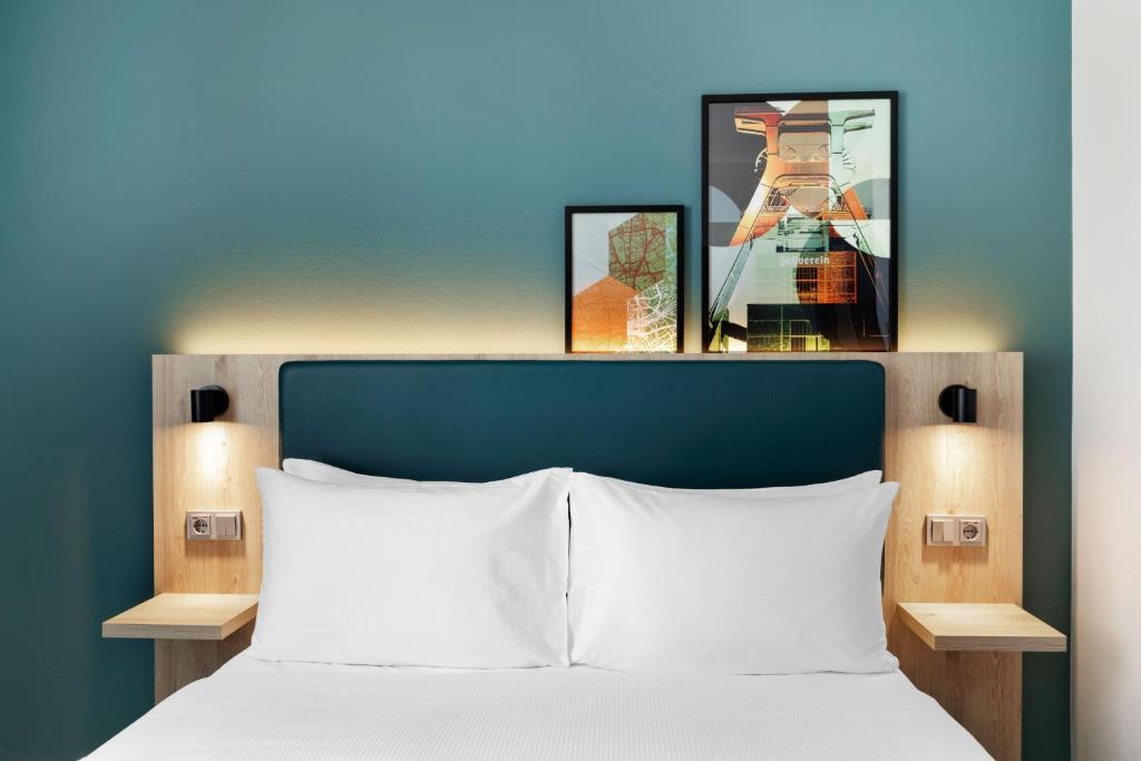 a bed with a blue headboard and two pictures above it at Spark by Hilton Essen City Centre in Essen