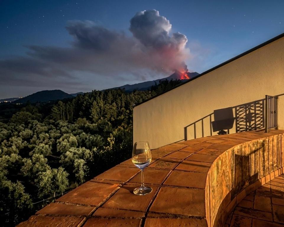 a wine glass sitting on top of a building with a fire in the background at Etna 1928 Country House in SantʼAlfio
