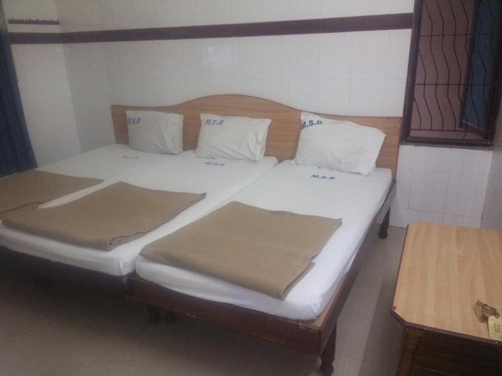 a bed with white sheets and pillows in a room at MSR Lodge in Tirupati