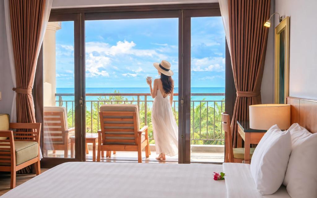 a woman standing on a balcony looking out at the ocean at Phu Hai Beach Resort & Spa Phan Thiet in Mui Ne