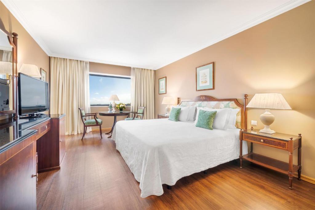 A classic bedroom with a large bed, window table and television.