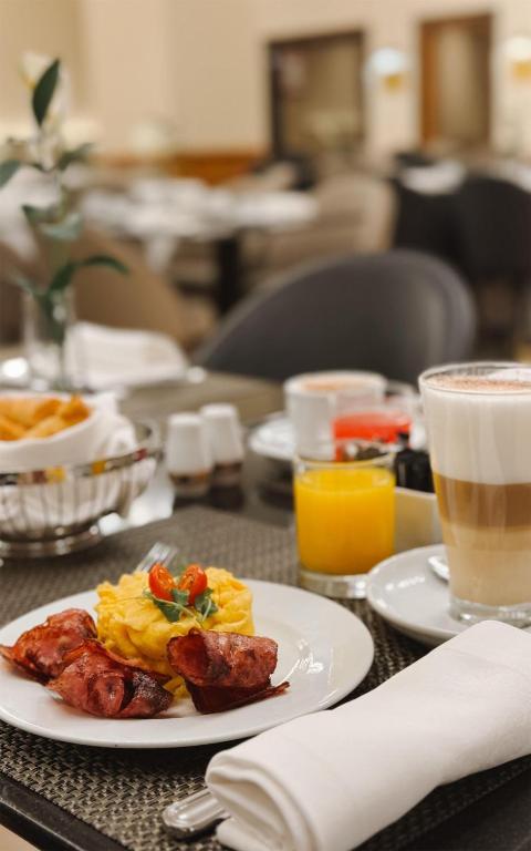 A plated breakfast includes eggs, sausages, orange juice and a latte.