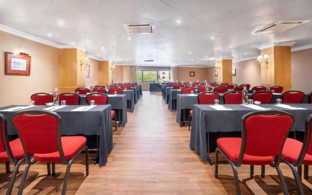 A long conference room arranged with rows of clothed tables and red chairs.
