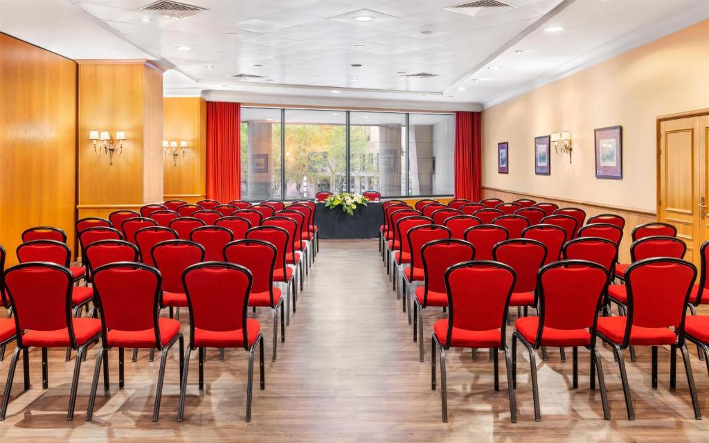 A large theatre-style auditorium with red chairs facing a windowed front wall.