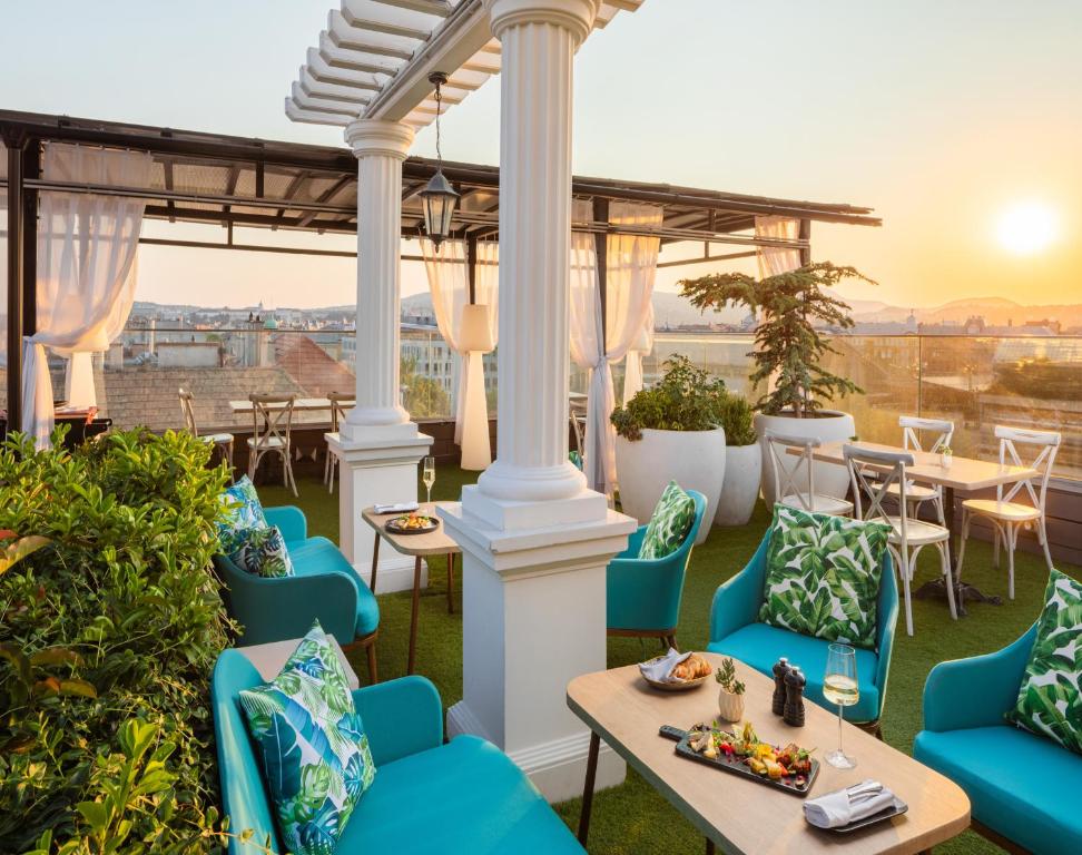 a patio with blue chairs and tables and the sunset at Mystery Hotel Budapest, Preferred Hotels & Resorts in Budapest